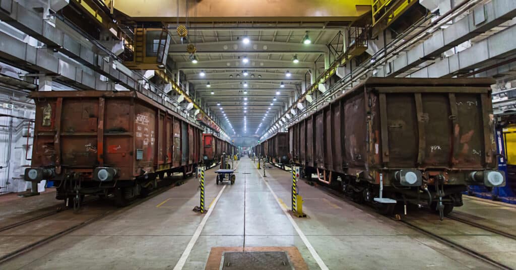 Two brown railcars lined up beside each other in a railcar maintenance facility.