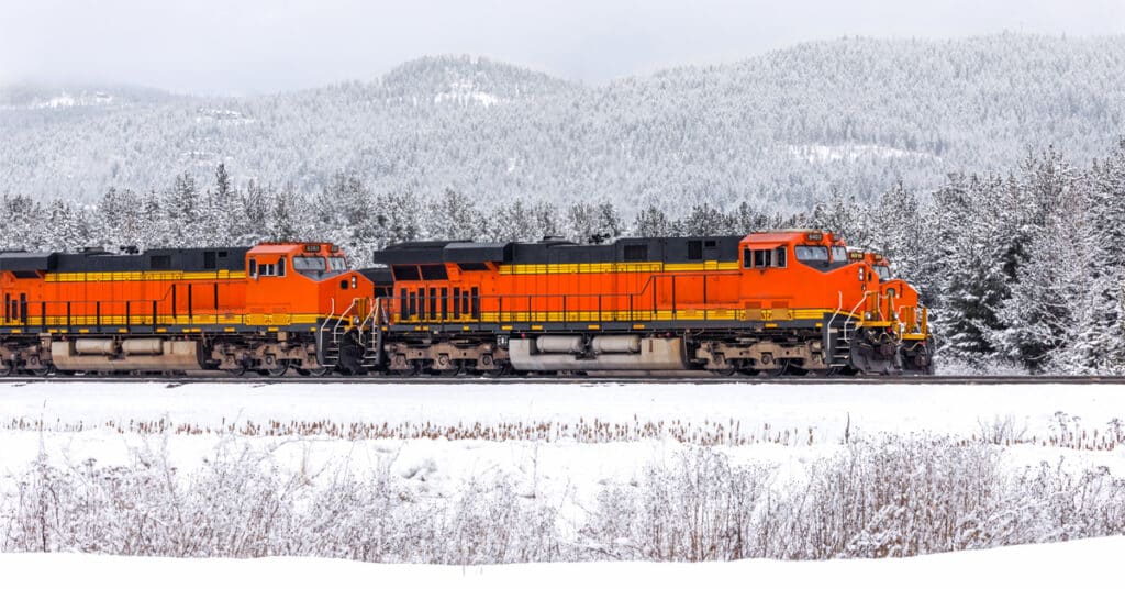 An orange rail freight engine in the middle of a snowy forest.