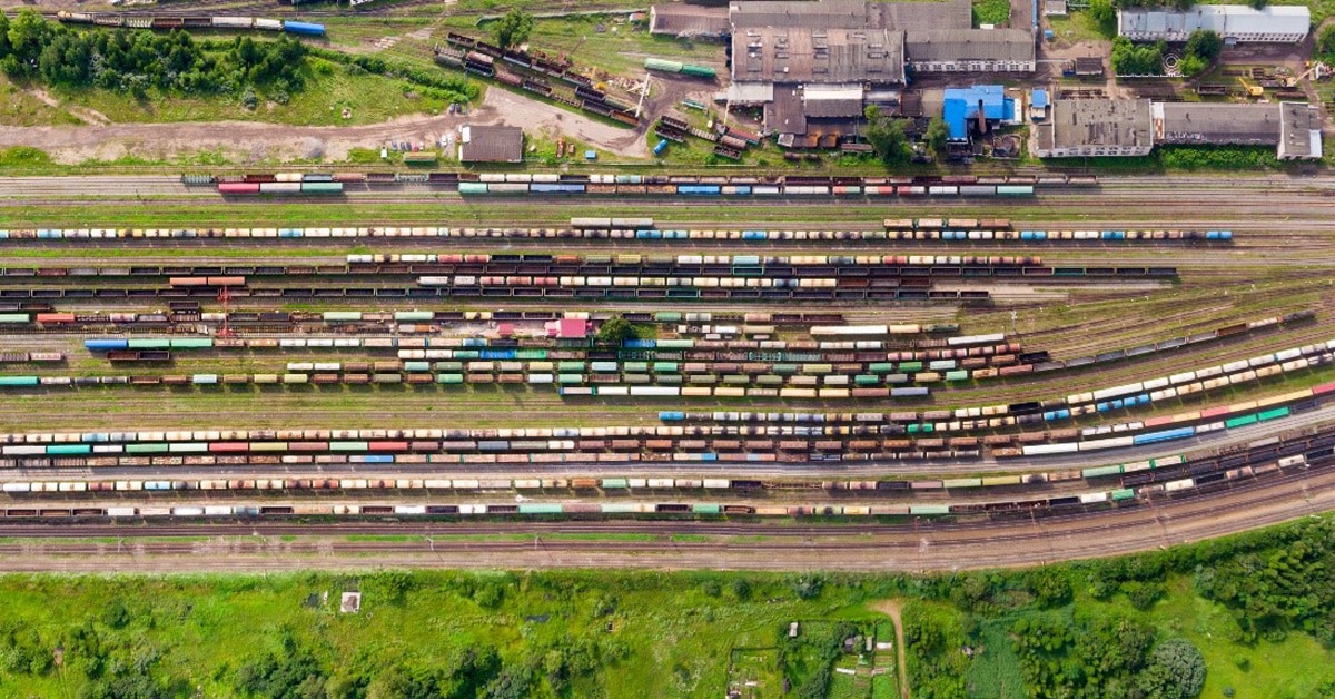 Vibrant rail yard with multiple train tracks crisscrossing each other, filled with colorful locomotives and cargo cars. 