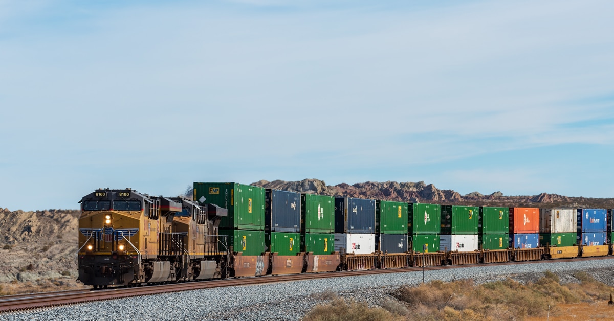 A yellow and blue freight train hauls a line of multicolored freight cars through a shrub desert.
