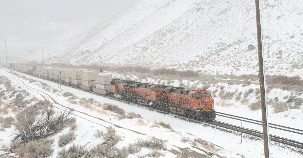 An orange BNSF train hauling white boxcars is moving through a snowy landscape.