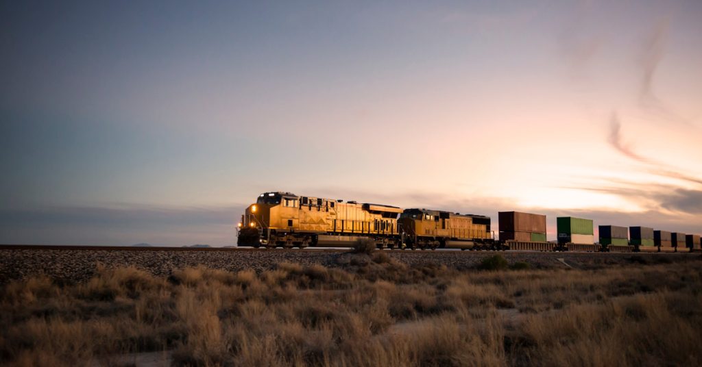 A yellow freight locomotive hauls railcars through a prairie. 