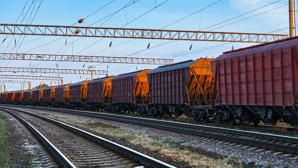 A lengthy line of railcars on a rail track in front of a blue sky and setting sun.