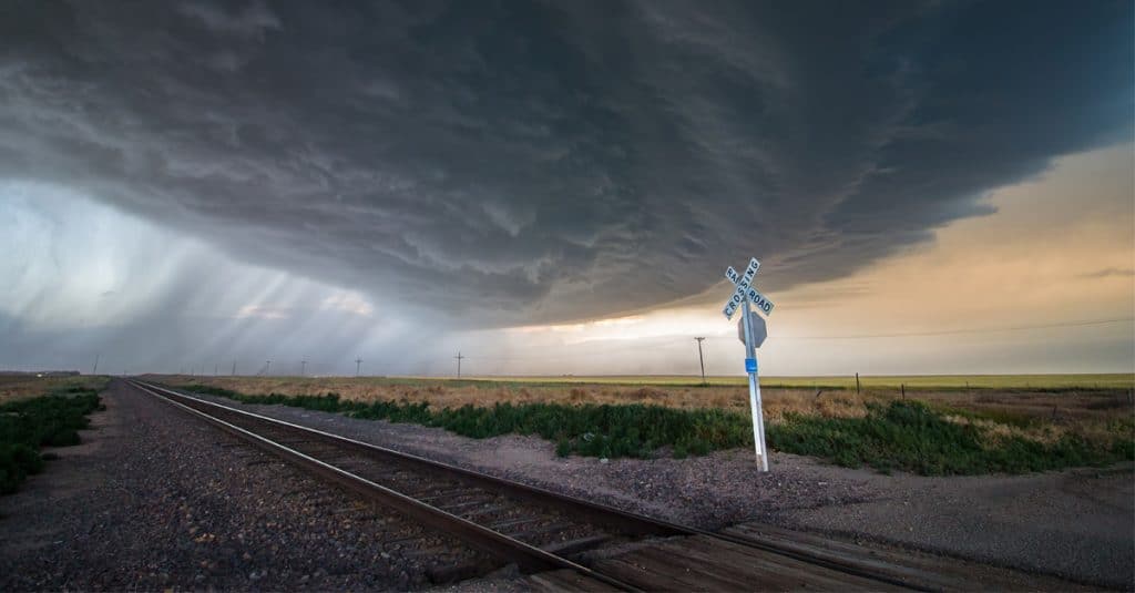 An incoming rail storm over a train track and railroad crossing sign.