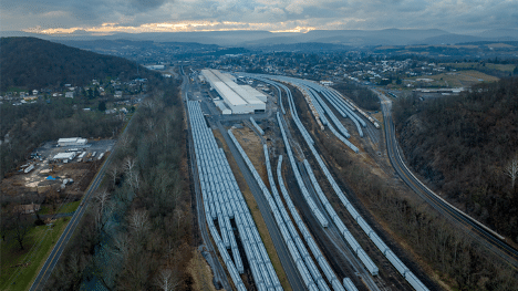 Aerial view of white rail cars lined up and waiting in a rail yard among trees and hills.