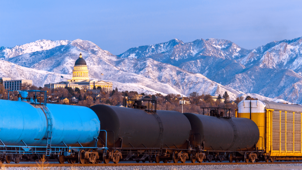Rail tank cars in front of the Salt Lake City skyline and snowcapped mountains.