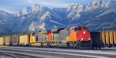 An orange and red colored class one railroads in front of a mountain range.