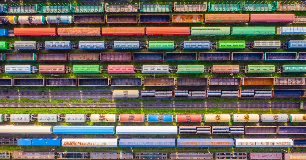 Top down view of a variety of colorful railcars in a railyard amongst green grass.