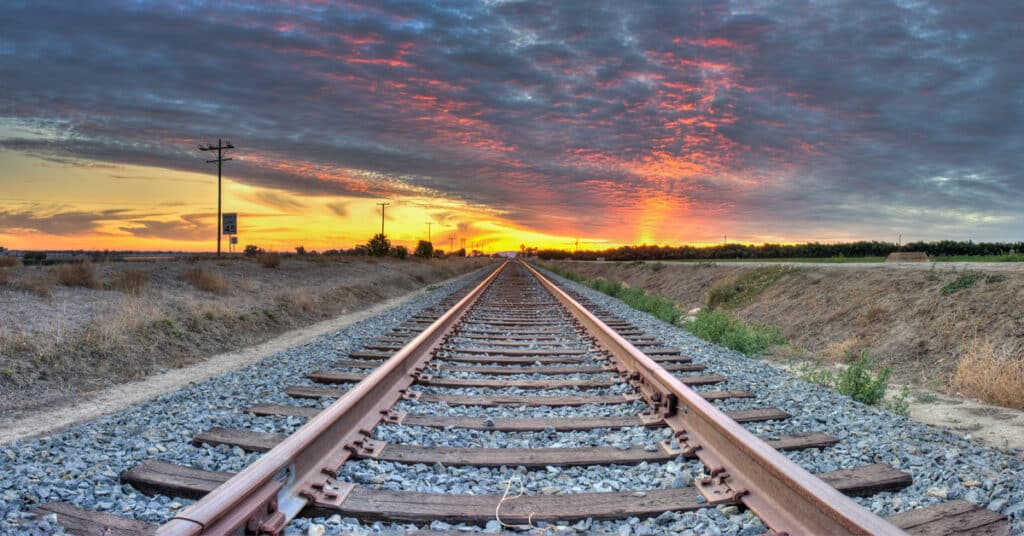 Panoramic view of railroad tracks crossing the frame on a prairie looking at a sunrise.