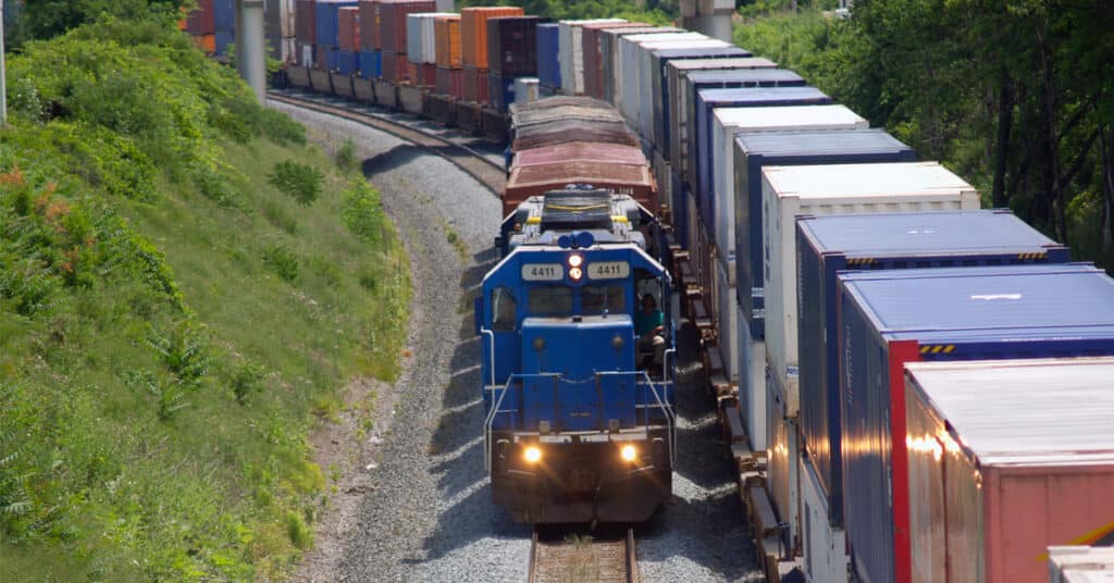 A blue locomotive pulling a short train beside parked container cars.