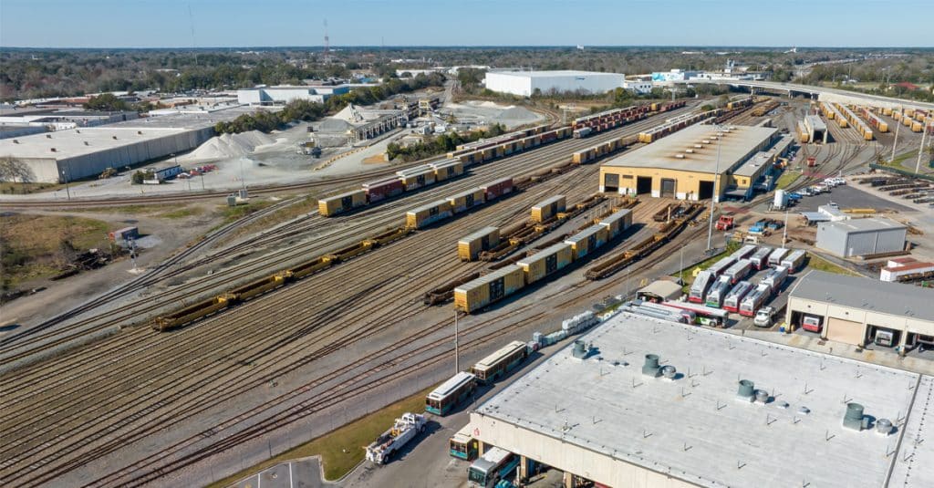 Aerial view of rail freight tracks, engines, and cargo alongside a factory and quarry.