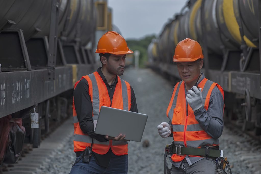 Workers with laptop on front of tank cars